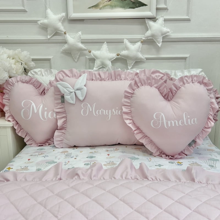 Personalizowana poduszka w kształcie serca w kolorze niebieskim z wyhaftowanym imieniem, otoczona innymi poduszkami w różnych kształtach i kolorach.