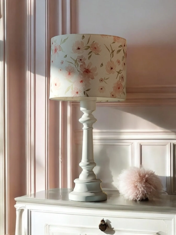 Stylowa biała lampa stołowa z klasyczną, ozdobną podstawą, wyposażona w abażur z kwiatowym wzorem w pastelowych odcieniach różu i zieleni